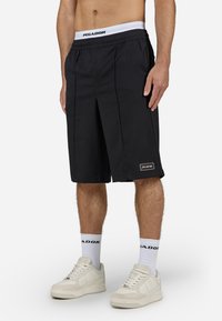 Shorts noirs avec un design plissé, fabriqués en tissu léger. Dotés d'une ceinture blanche avec logo de marque et d'un logo brodé sur l'ourlet.