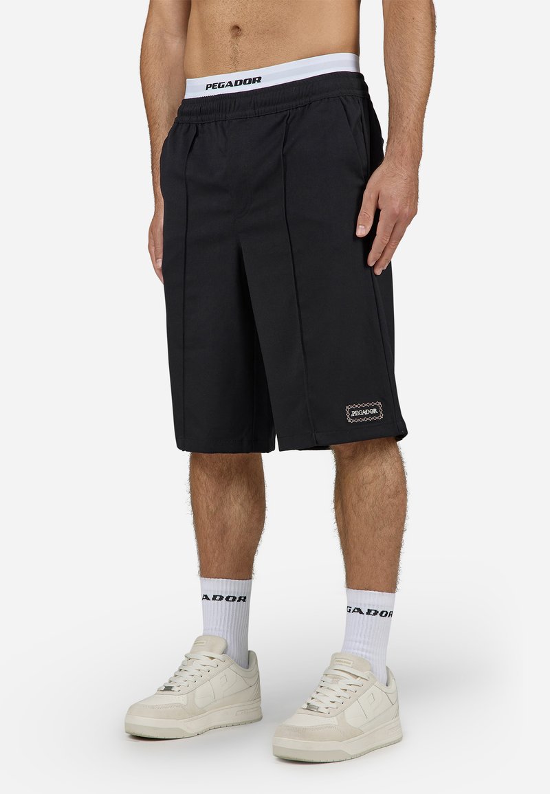 Shorts noirs avec un design plissé, fabriqués en tissu léger. Dotés d'une ceinture blanche avec logo de marque et d'un logo brodé sur l'ourlet.
