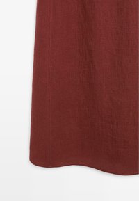 Saum eines dunkelroten, strukturierten Stoffrocks mit leichter Wellenform vor weißem Hintergrund.