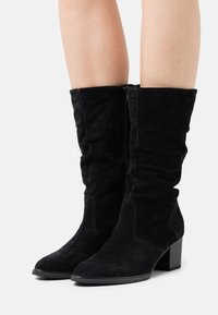 Bottes noires en daim hauteur genou avec un design décontracté, un talon bloc et une fermeture éclair sur le côté. Caractéristiques : texture lisse et bout pointu.