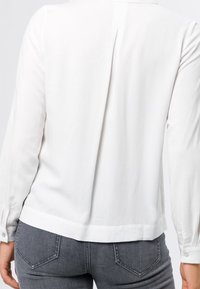 Witte blouse met lange mouwen van gladde stof, met een rugplooidetail. Voorzien van knoopmanchetten en een ronde zoom.