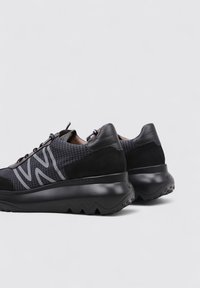 Sneaker nere con un upper in tessuto texturizzato, dettagli in pelle, un logo grigio distintivo e un design della suola spesso e frastagliato.