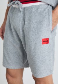 Graue Shorts aus weichem Stoff, mit einem roten Etikett mit "HUGO". Das Design umfasst einen elastischen Bund mit Kordelzug.