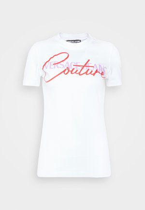 Biały t-shirt z krótkim rękawem i okrągłym dekoltem z napisem „Versace Jeans Couture” w fioletowym i czerwonym kolorze na piersi, na jednolitym tle.