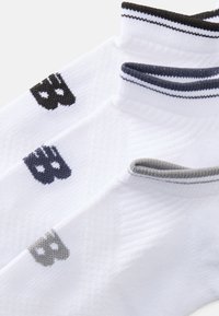Chaussettes de sport blanches avec des accents de logo noirs, navy et gris. Le design comprend des bords côtelés et un tricot texturé pour plus de confort.