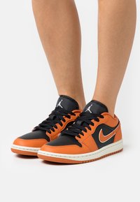 Baskets en cuir noir et orange à tige basse, avec une semelle intercalaire blanche, des lacets noirs et un logo Nike swoosh argenté.