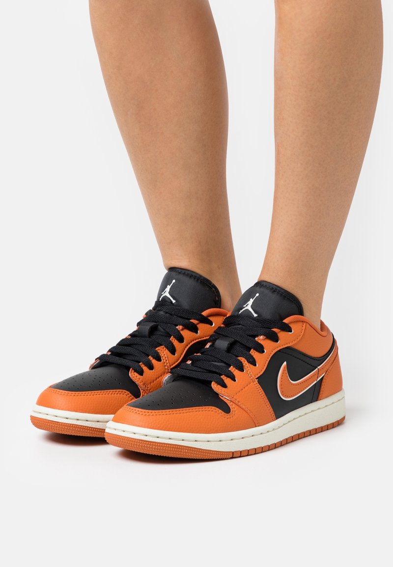 Baskets en cuir noir et orange à tige basse, avec une semelle intercalaire blanche, des lacets noirs et un logo Nike swoosh argenté.
