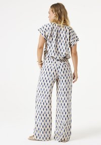 Twee-delig outfit in lichte stof, bestaande uit een kortmouwtop en een ruime broek. Bedrukt met blauwe druppelvormen op een beige achtergrond.