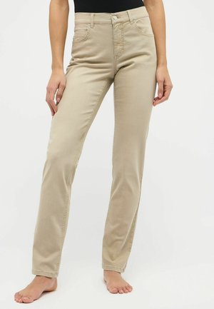 Beige Baumwoll-Hosen mit geradem Bein und mittelhohem Bund, frontalen Taschen und einem sauberen Abschluss am Saum, präsentiert an einem barfuß stehenden Modell.