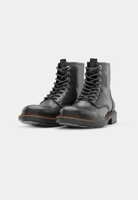 Botas de cuero negras con un diseño de cordones, superficie texturizada y un acento marrón a lo largo de la suela. Suela de goma gruesa para mayor agarre.