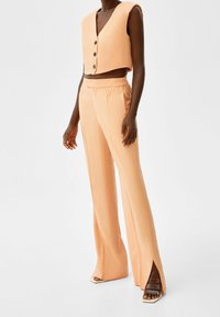 Peach cropped vest with buttons and matching high-waisted trousers featuring side slits. Material appears lightweight and smooth.