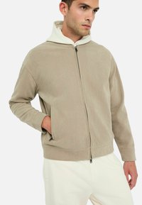 Beige corduroy zip-hoodie med store forlommer og en hvid inderside, med et afslappet fit og ribbede manchetter.