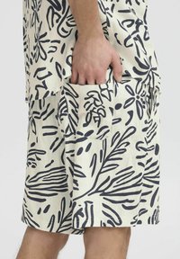 Pantalones cortos de lino con un fondo crema y un diseño de hojas en negrita en color azul marino, con bolsillos laterales y un corte relajado.