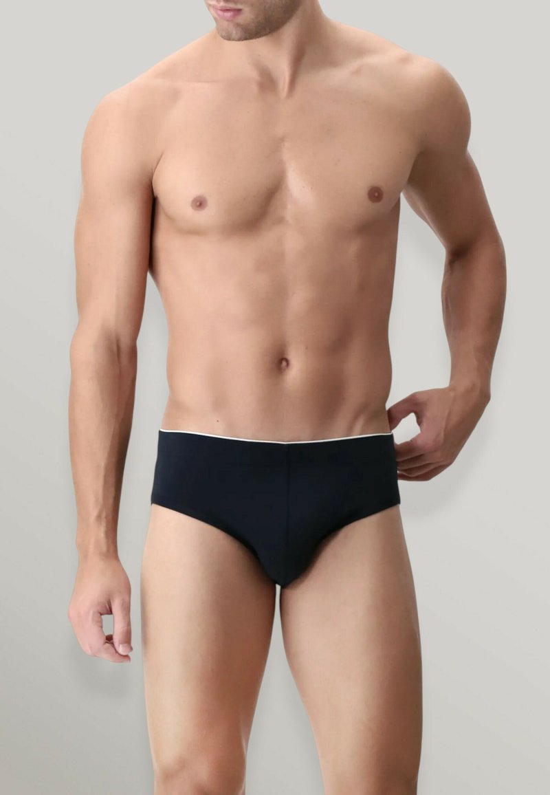 Costumi da bagno neri da uomo con un bordo bianco in vita. Tessuto liscio, forma aderente e design a vita bassa. Stile minimalista.