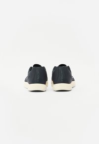 Baskets noires avec une finition texturée, dotées d'une semelle en caoutchouc blanche et d'un logo à l'arrière. Design minimaliste, style bas.