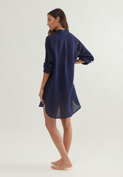 Tengerészkék len ingruha felhajtott ujjakkal, ívelt szegéllyel és oldalsó hasítékokkal. Könnyű anyagból, laza fazonban.
