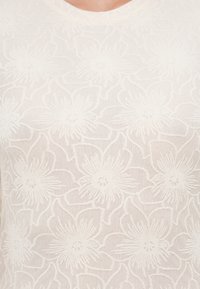 Επάνω μέρος από λευκόχρυση δαντέλα με υφή και μεγάλο σχέδιο λουλουδιών με διακριτικές λεπτομέρειες, κατασκευασμένο από διαφανές, αεριζόμενο ύφασμα.