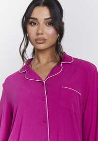 Camisón magenta con textura acanalada, con ribete blanco en el cuello y el bolsillo, y cierre de botones. Incluye un bolsillo en el pecho.