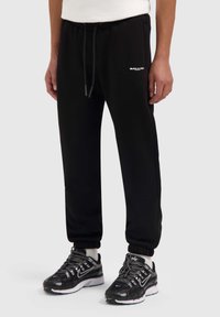 Zwarte joggingsbroek van zachte stof, met een tailleband met trekkoord, elastische boorden en een klein wit "BALLIN'" logo aan de voorkant.