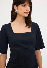 Top blu navy con scollatura quadrata, maniche corte e pannellatura testurizzata lungo il torso; tessuto liscio con dettagli di design minimi.