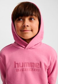 Rosa Kapuzenpullover mit einer Kängurutasche vorne und einem erhabenen Logo "hummel SPORTSWEAR" in der Mitte der Brust. Weicher, strukturierter Baumwollmischstoff.