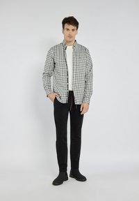 Koszulka w kratę w kolorze czarnym, białym i szarym, zapinana na guziki, noszona rozpięta na białej koszulce; zestawiona z czarnymi, slim-fit spodniami i czarnymi butami.