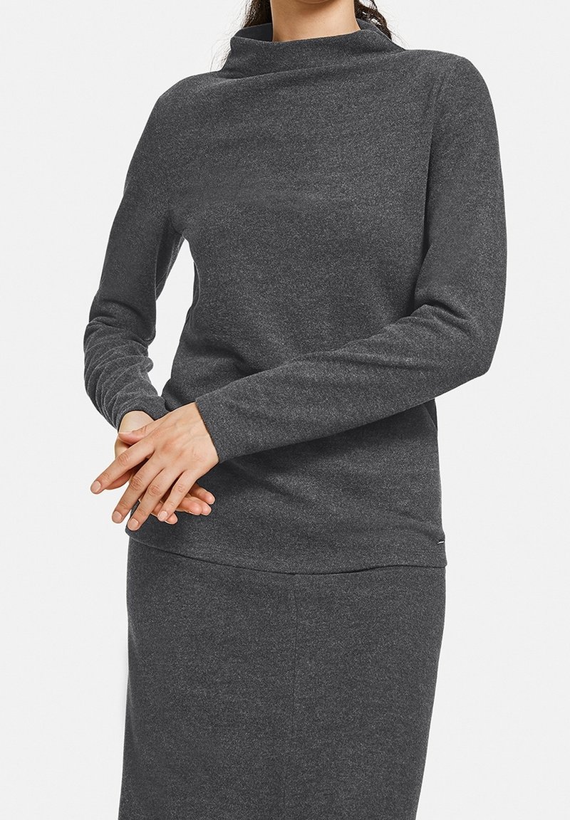 Dunkelgraues Langarmshirt mit hochgeschlossenem Kragen, aus weichem, strukturiertem Stoff gefertigt. Verfügt über enganliegende Ärmel und einen abgerundeten Saum.
