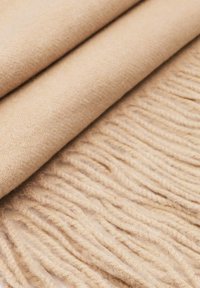 Coperta in lana beige con una superficie morbida e texturizzata; i bordi frangiati creano un aspetto a strati, esaltando il suo aspetto accogliente.