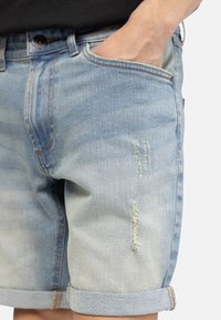 Hellblaue Denim-Shorts mit einem verwaschenen Finish, ausgestattet mit Used-Effekten und umgeschlagenen Säumen. Enthält Vordertaschen und einen Knopfverschluss.