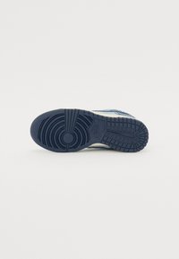 Nike-sko med en struktureret marineblå gummisål, kontrastfyldt lyseblå overdel af ruskind og et fremtrædende cirkulært dækmønster.
