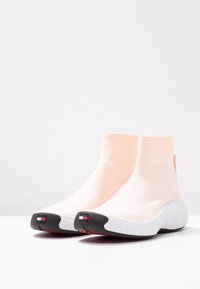 Hoge sneakers in zacht perzikstof met een geribbelde enkelsok, witte tussenzool en een contrasterende zwarte zool met een logoaccent.