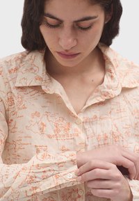 Camicia button-up beige chiaro con stampa mappale arancione su tutta la superficie, che include isole ed elementi marini; texture morbida e colletto classico.