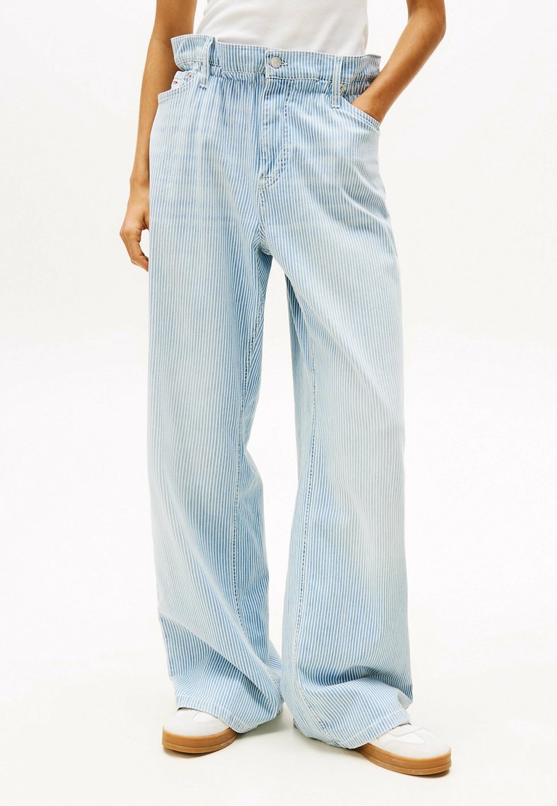 Pantalones de pierna ancha hechos de una tela a rayas de color azul claro con un acabado texturizado. Cuenta con una cintura alta y bolsillos laterales. Llevados con calzado blanco.