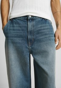 Ljust blå denimjeans med avslappnad passform, som har en medelhög midja, subtil blekning och kontrastsömmar längs sömmarna.