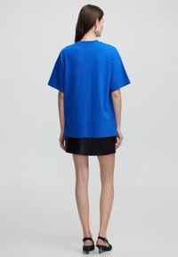 Blauwe katoenen T-shirt met korte mouwen en een ontspannen pasvorm, gecombineerd met een zwarte leren minirok, gezien van achteren.