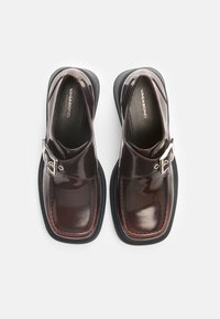 Brown patent leather shoes with a rounded toe, thick black sole, and silver buckle detail. Smooth texture and minimalist design.