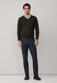 Mörkgrön v-ringad tröja i kombination med en ljusblå skjorta med krage, marinblå byxor och bruna snörskor. Enkelt, klassiskt design.