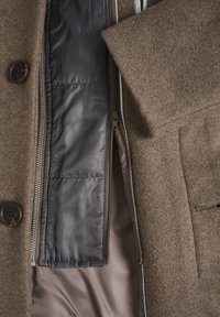 Brauner Wollmantel mit Reißverschluss vorne und satinähnlichem Futter. Verfügt über einen Knopfverschluss und eine Tasche mit Klappe. Das Innere hat eine steppte Detail.
