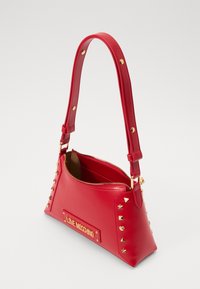 Rote lederne Handtasche in dreieckiger Form, mit goldenen Hardware-Akzenten, Reißverschluss und Nietenverzierungen. Verfügt über ein Logo-Schild.