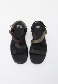 Crne i maslinasto zelene sandale s prilagodljivim tekstilnim trakama, koje imaju podstavljeni đon i gumeni potplat. Vidljivi logotipi "CAMPER" i "TWINS".