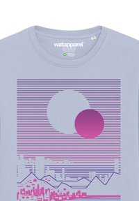 Lichtblauwe t-shirt met een grafisch ontwerp van een grote witte cirkel en een kleinere roze cirkel, met horizontale lijnen en een bergsilhouet.