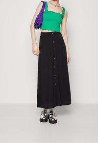 Vihreä smokkikroppitoppi röyhelöreunuksilla, musta maksihame nappien kanssa edessä ja hopeiset paksupohjaiset kengät remmeillä.