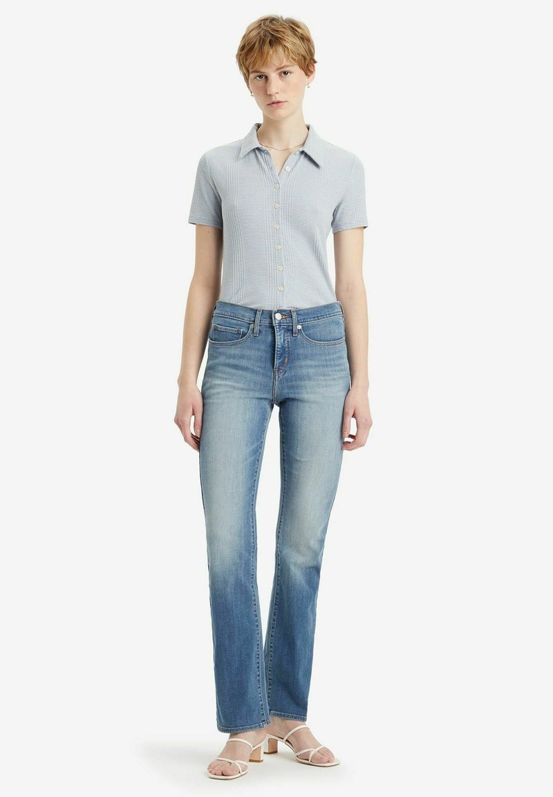 Camisa polo de manga corta azul claro con botones, combinada con jeans rectos de mezclilla desgastados y sandalias blancas de tiras.