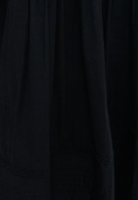 Μαύρο ύφασμα με απαλά πτυχώσεις και διακριτικές ραμμένες οριζόντιες γραμμές κοντά στην κάτω άκρη.