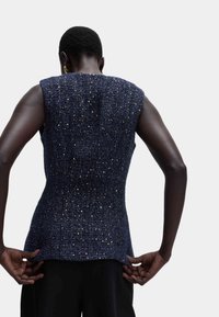 Marineblauw mouwloos topje met een gestructureerd patroon met metalen draden. Strak passend ontwerp met een rechte zoom aan de onderkant.