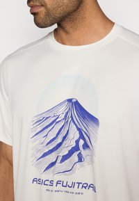 T-shirt de sport blanc présentant un graphique bleu d'une montagne avec le texte « ASICS FUJITRAIL », doté d'un col rond et d'un tissu texturé.