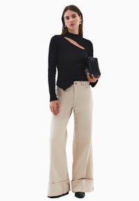 Czarny długi rękaw bluzka z wycięciem; beżowe szerokie spodnie dżinsowe; trzyma małą,teksturalną czarną torebkę; czarne obuwie.