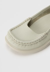 Chaussure slip-on en cuir gris clair avec un bout rond, une tige texturée et des coutures contrastantes le long du bord. Semelle extérieure en caoutchouc plate.
