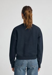 Mörk marinblå sweatshirt med lång ärm, rund halsringning och ribbade muddarna. Mjuk textur och avslappnad passform. Stylen kombineras med blå jeans.