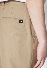 Khaki pants made of durable fabric, featuring a back pocket with a black Nike logo tag and a smooth, lightly textured surface.